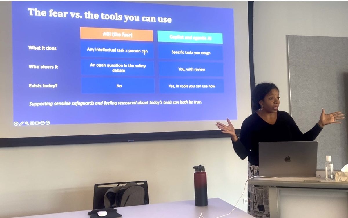 Sebrina Williams teaching a workshop, beside a slide comparing the fear of AGI with the AI tools businesses can actually use today.